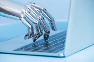 A chrome robotic hand typing on a laptop keyboard