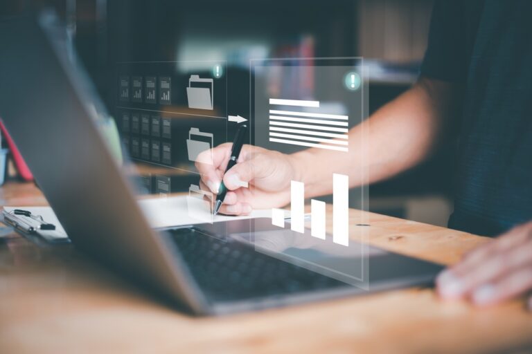 A person writing beside a laptop with document and bar chart graphics overlaid